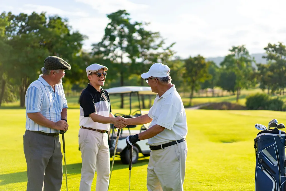 Trois golfeurs seniors se serrant la main sur le parcours, aspect social du golf après 50 ans
