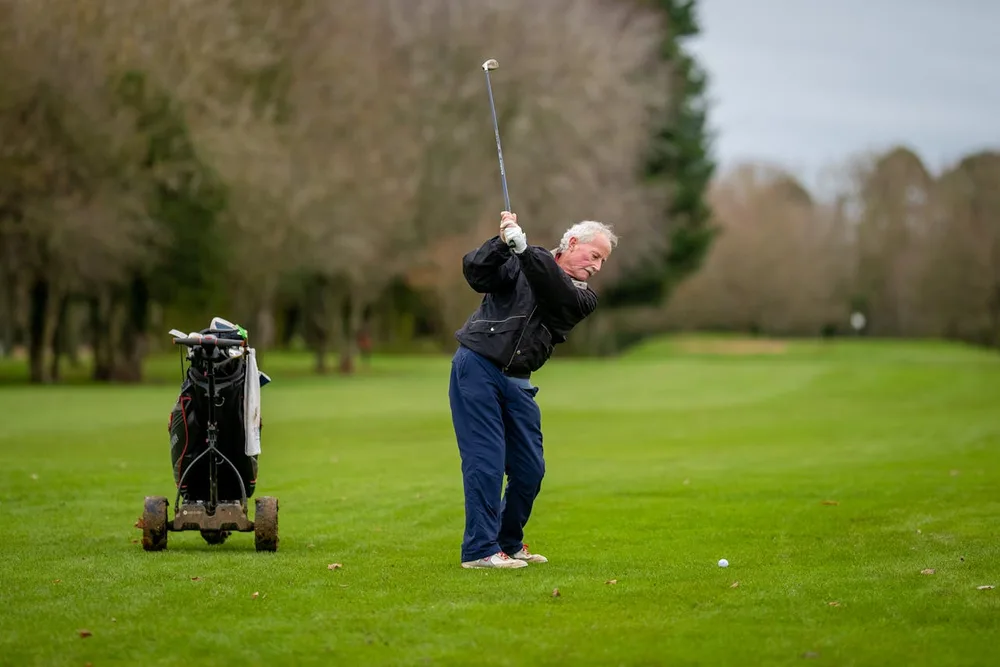 Golfeur senior en plein swing sur parcours verdoyant, arthrose et golf compatibles