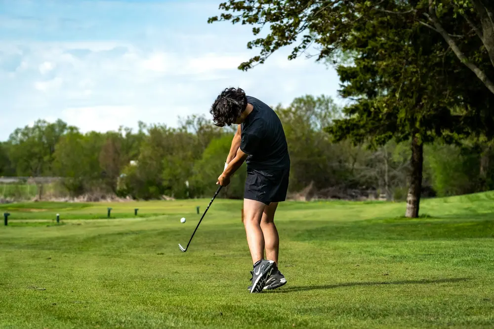 Jeune golfeur débutant frappant une balle sur parcours, premier achat clubs golf