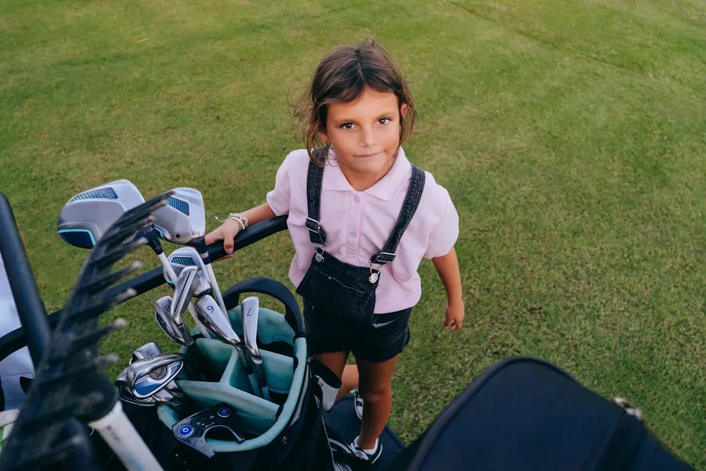 Petite fille de 6 ans avec son sac de clubs junior sur le parcours, kit golf enfant taille adaptée