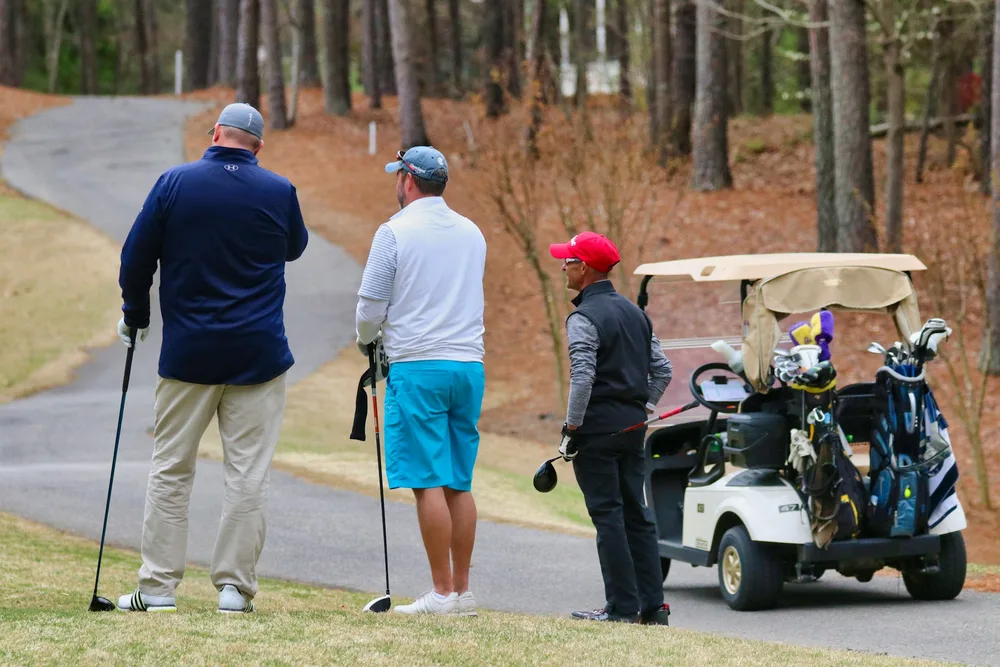 Équipe de trois golfeurs en scramble attendant leur tour sur le parcours avec voiturette
