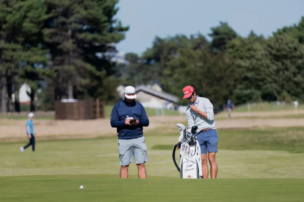 Deux golfeurs en scramble consultant la carte de score et discutant de la stratégie sur le fairway