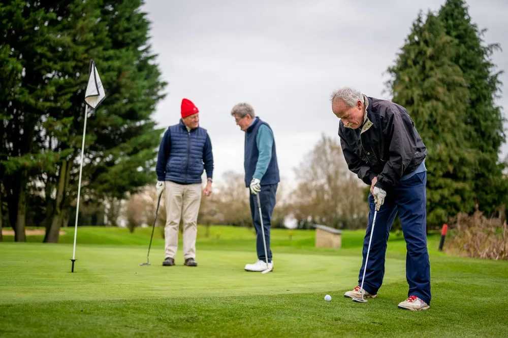 Trois golfeurs seniors jouant ensemble sur un green, illustration du lien social au golf après 70 ans