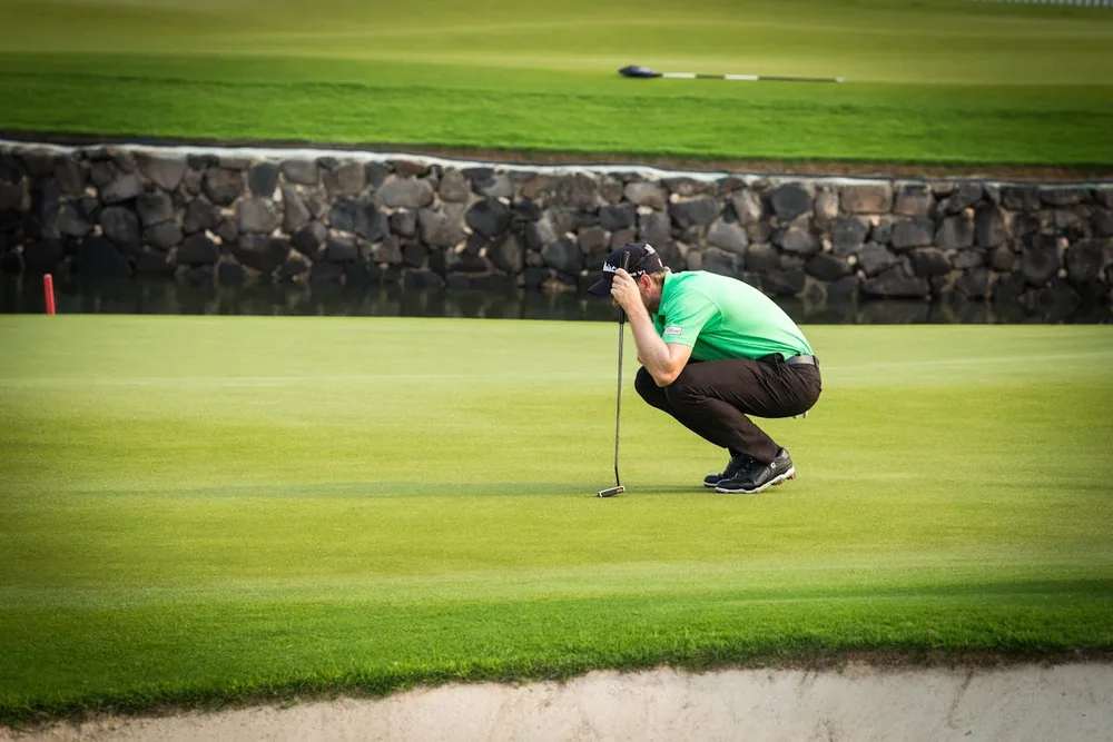 Golfeur accroupi lisant les pentes d'un green au bord d'un bunker, illustration de la lecture de green au golf