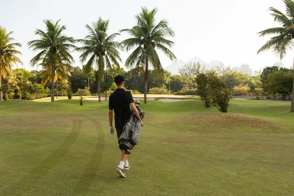 Golf avion : un joueur porte un sac de golf sur un parcours bordé de palmiers.