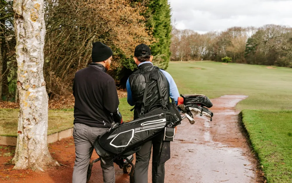 Golf en hiver : deux golfeurs marchent avec un sac sur un parcours bordé d'arbres.