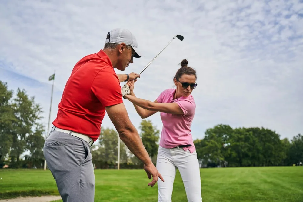 Initiation au golf avec un instructeur qui accompagne une débutante dans son geste